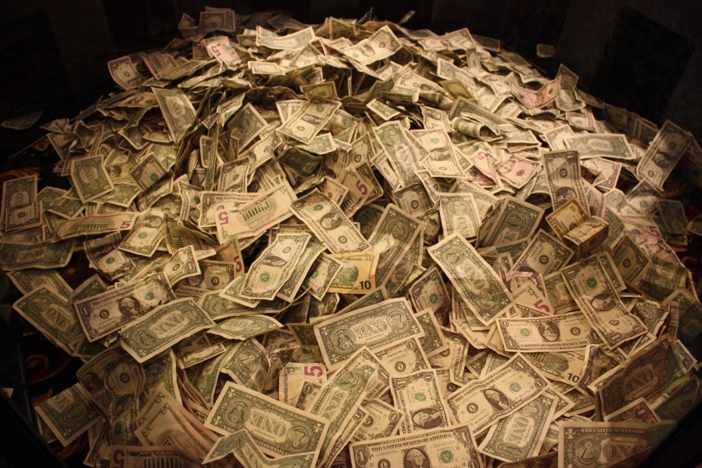 A large pile of crumpled US dollar bills scattered across a dark surface.