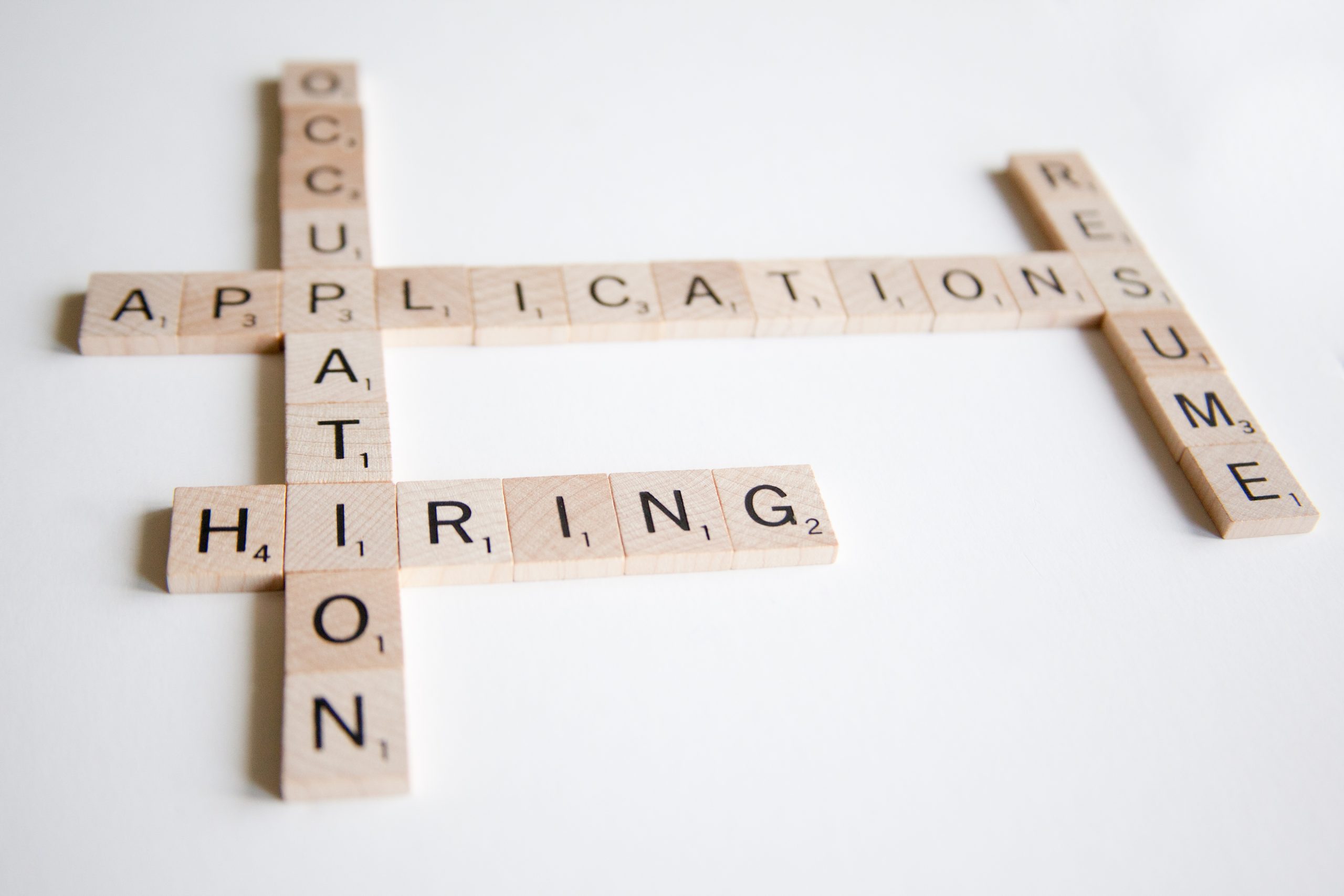 Wooden letter tiles forming a crossword with the words occupation, application, resume, and hiring.
