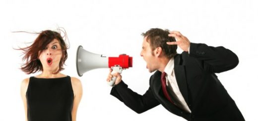 A man in a suit shouts through a megaphone at a startled woman whose hair is blowing back.
