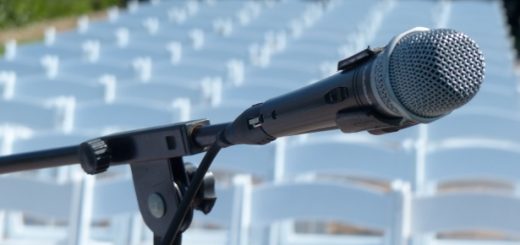 A microphone on a stand in front of rows of empty white chairs outdoors.