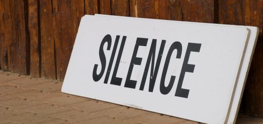 A white rectangular sign with the word SILENCE leaning against a rustic wooden wall.