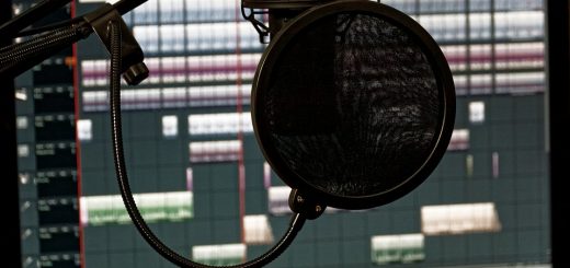A studio microphone with a pop filter in front of a computer monitor displaying audio tracks.