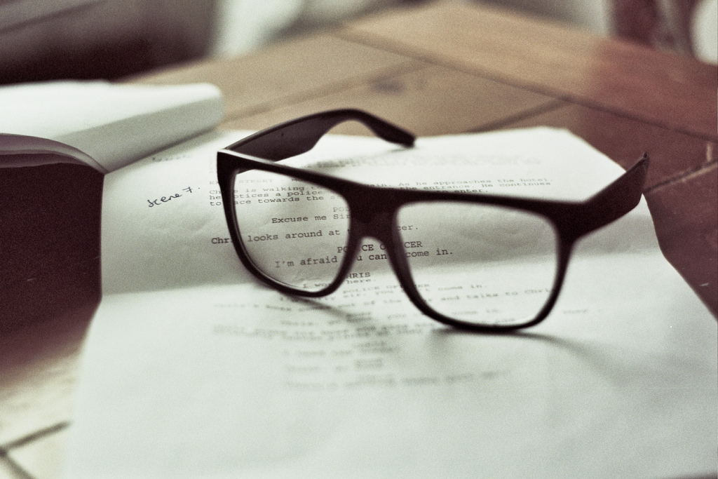 Black-rimmed glasses resting on a printed script on a wooden table.