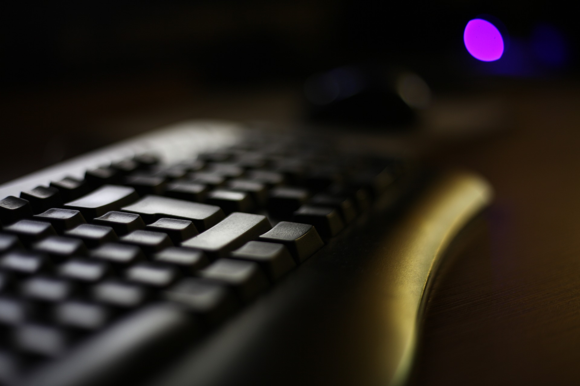 Close-up of a black computer keyboard on a desk in dim lighting.