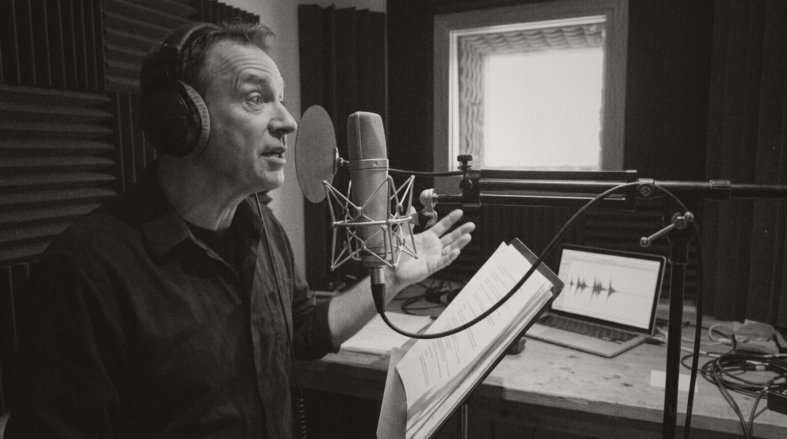 A voice actor mid-performance in a recording booth, expressive and reading from a script © The Voice Realm
