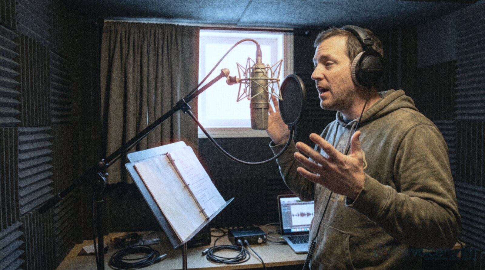 A voice actor in a hoodie performing a script with big gestures at a booth mic © The Voice Realm