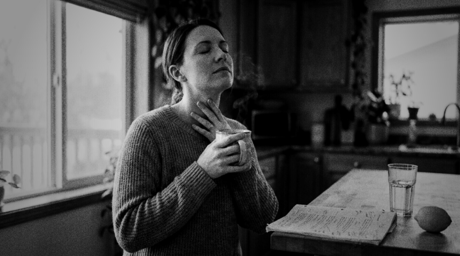 A voice actor at her kitchen window in the morning, eyes closed, humming gently with a hand on her throat and a mug of tea, a marked-up script on the counter © The Voice Realm