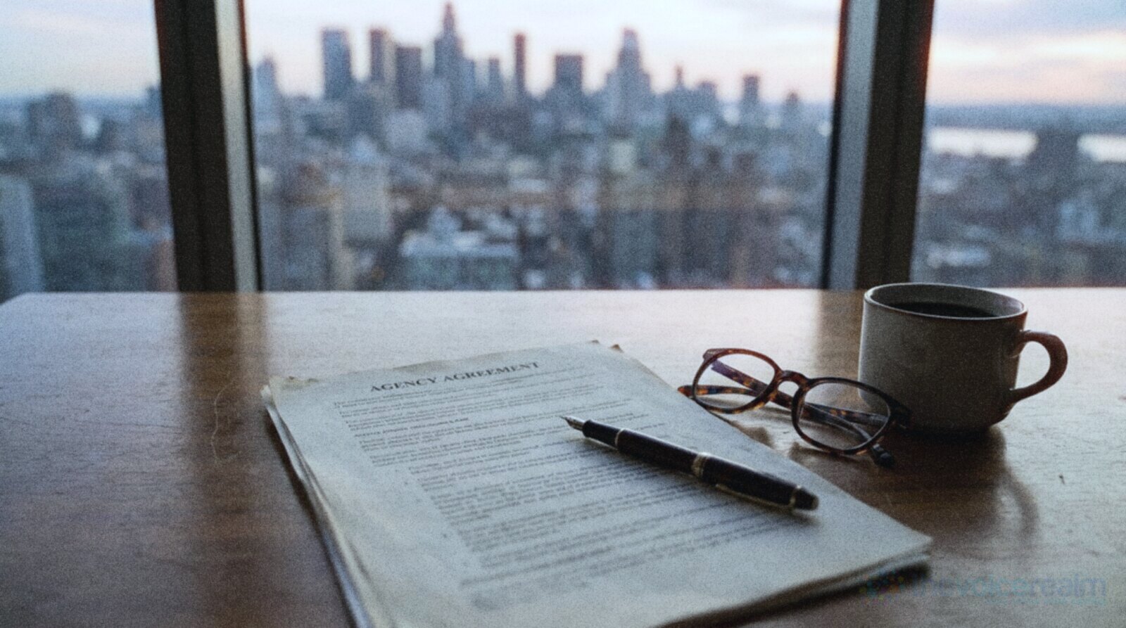 An agency agreement on a wooden desk with a fountain pen, reading glasses and a coffee, a city skyline through the window © The Voice Realm
