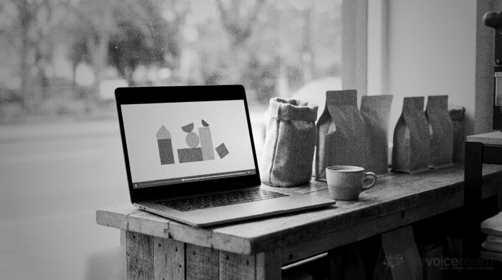 A laptop on a coffee roaster's wooden counter playing a simple animated explainer video, beside bags of coffee beans and a cup of coffee © The Voice Realm