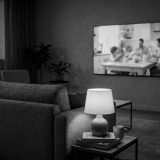 A living room at evening seen from behind a sofa, a wall television showing a family breakfast commercial © The Voice Realm