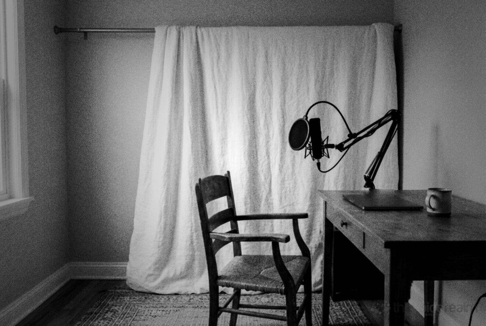 A thick white duvet hung from a curtain rail a little way off a bedroom wall, behind a wooden chair, with a microphone on a desk arm in front © The Voice Realm