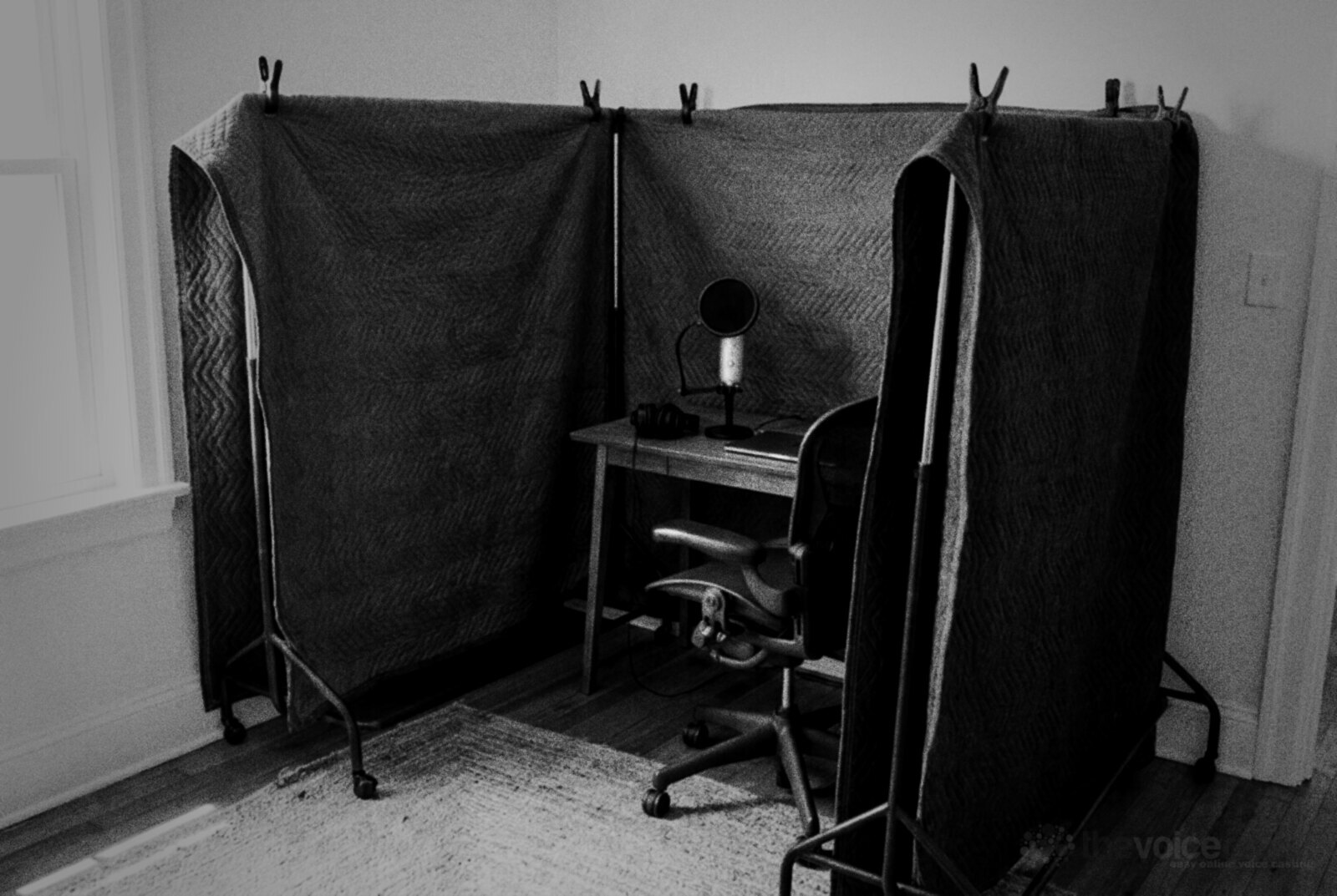 Grey quilted moving blankets clipped over two freestanding clothes rails in a U shape around a small desk, office chair and microphone © The Voice Realm