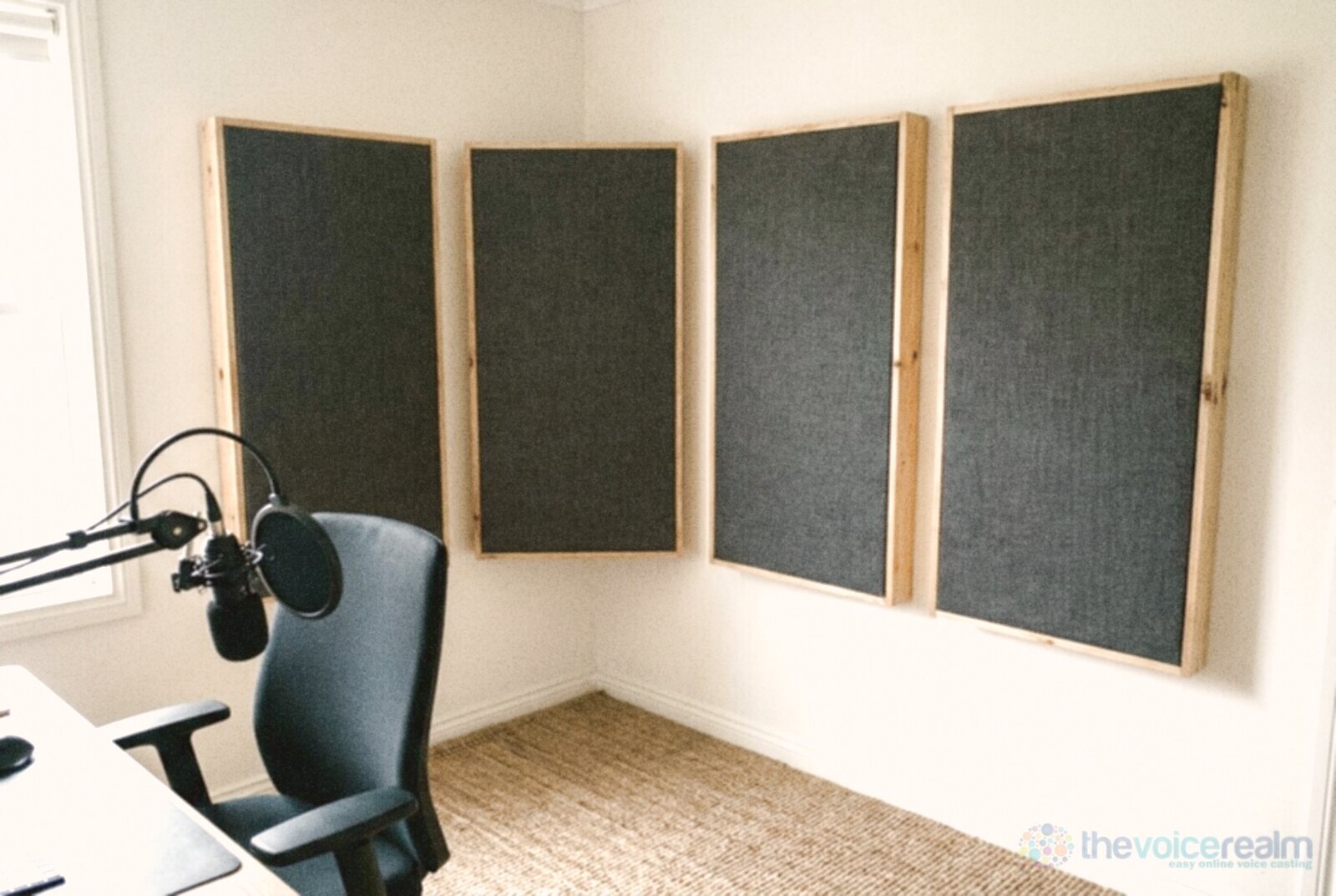 Four home-made acoustic panels, pine frames wrapped in charcoal fabric, hung across a room corner behind an office chair and microphone © The Voice Realm