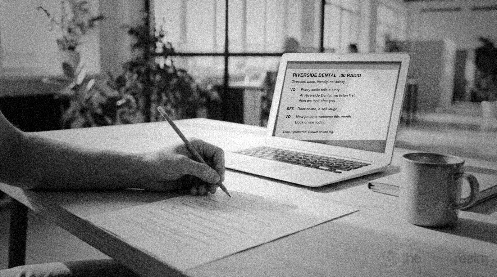 A hand writing pencil notes on a printed script beside an open laptop and a coffee mug in a bright office © The Voice Realm