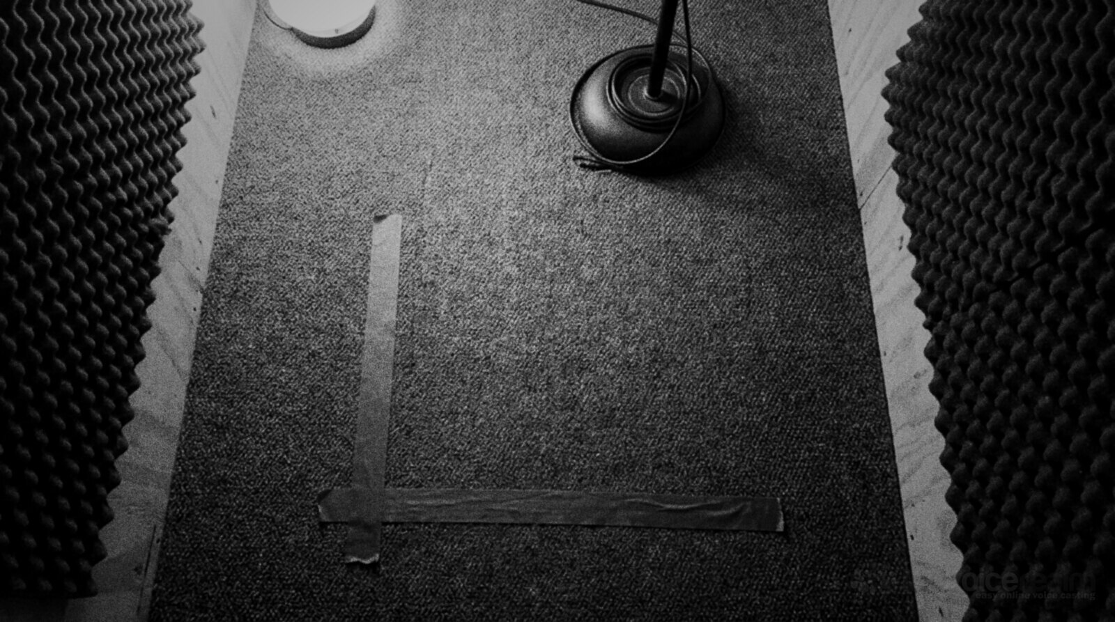 Black and white photo of a home recording booth floor with an L of tape marking where the narrator's feet go, foam panels on both walls and a mic stand base © The Voice Realm