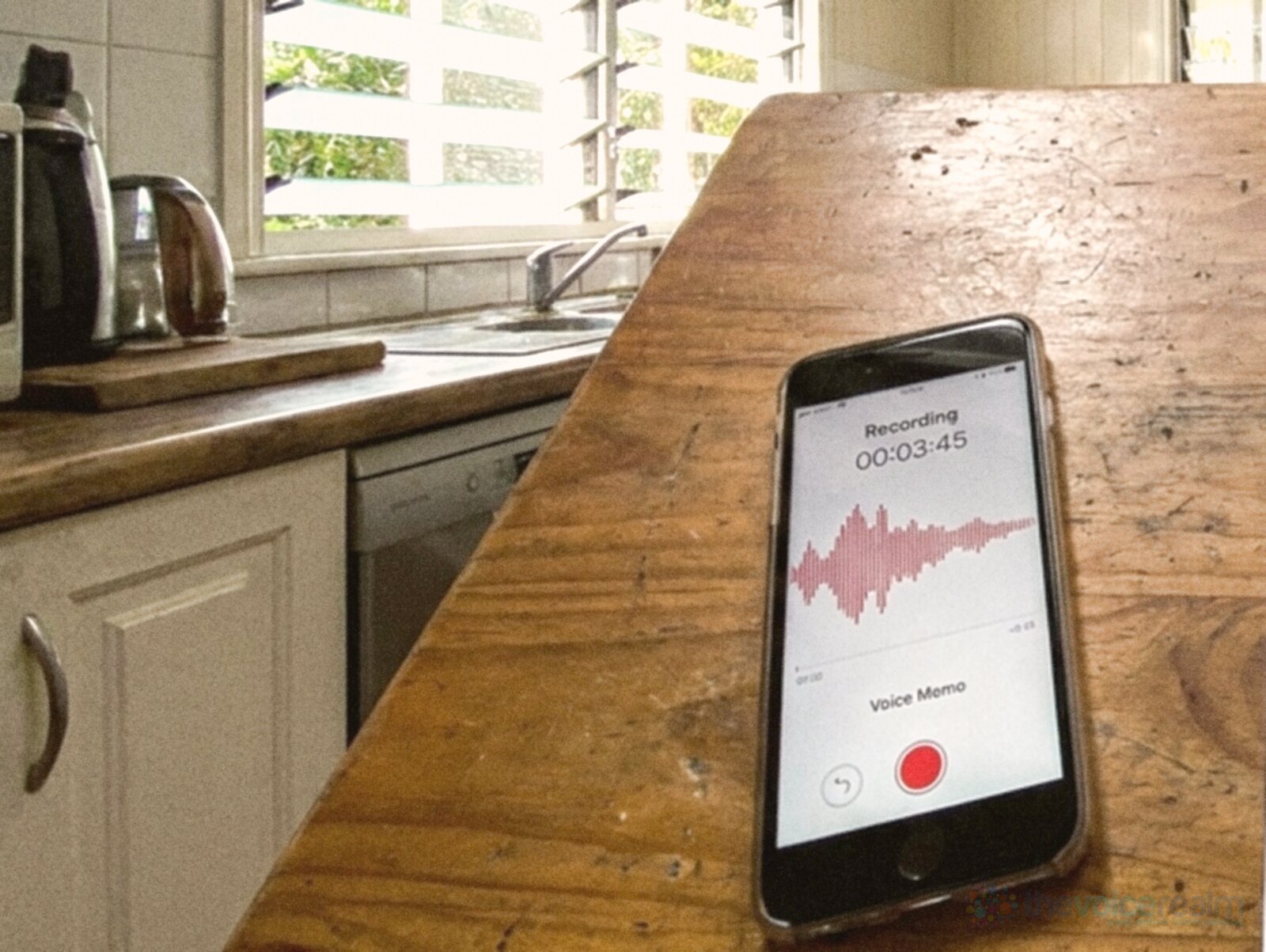 A smartphone recording a voice memo on the worn timber kitchen bench of an old Queensland house with louvre windows © The Voice Realm