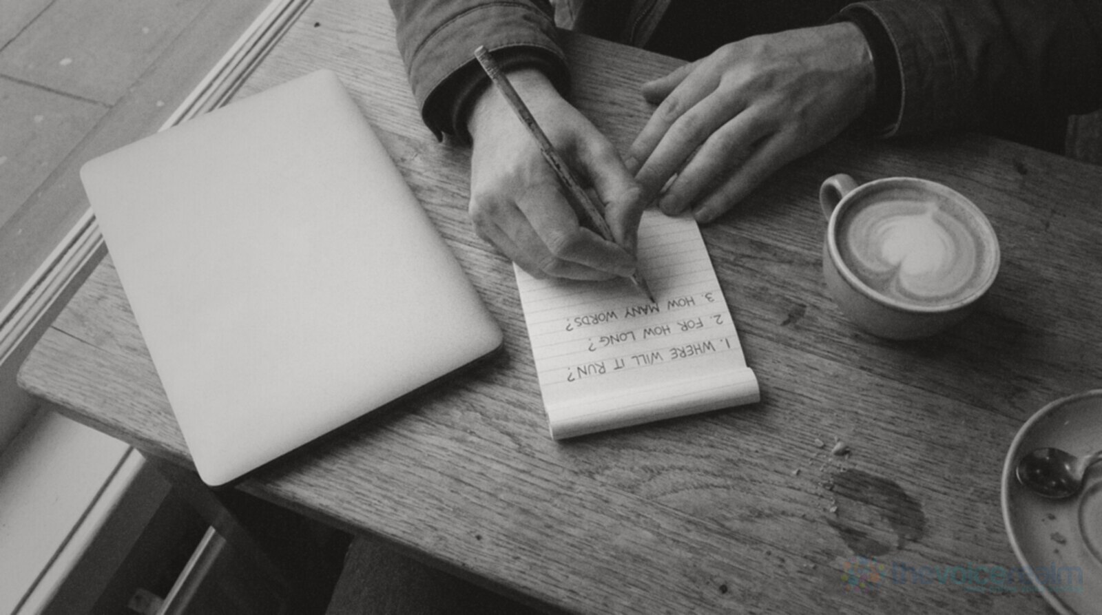 Hands writing three questions in pencil on a small notepad at a cafe table, where will it run, for how long and how many words, beside a closed laptop and a flat white, black and white photograph © The Voice Realm
