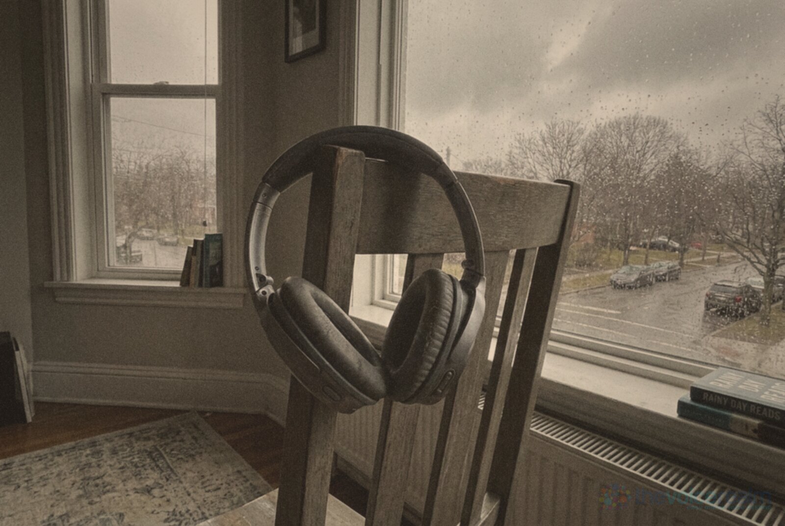 A pair of over-ear headphones hanging on the corner of a wooden chair beside a rain-streaked window looking over a wet street on a grey afternoon, in faded 1970s print colours © The Voice Realm