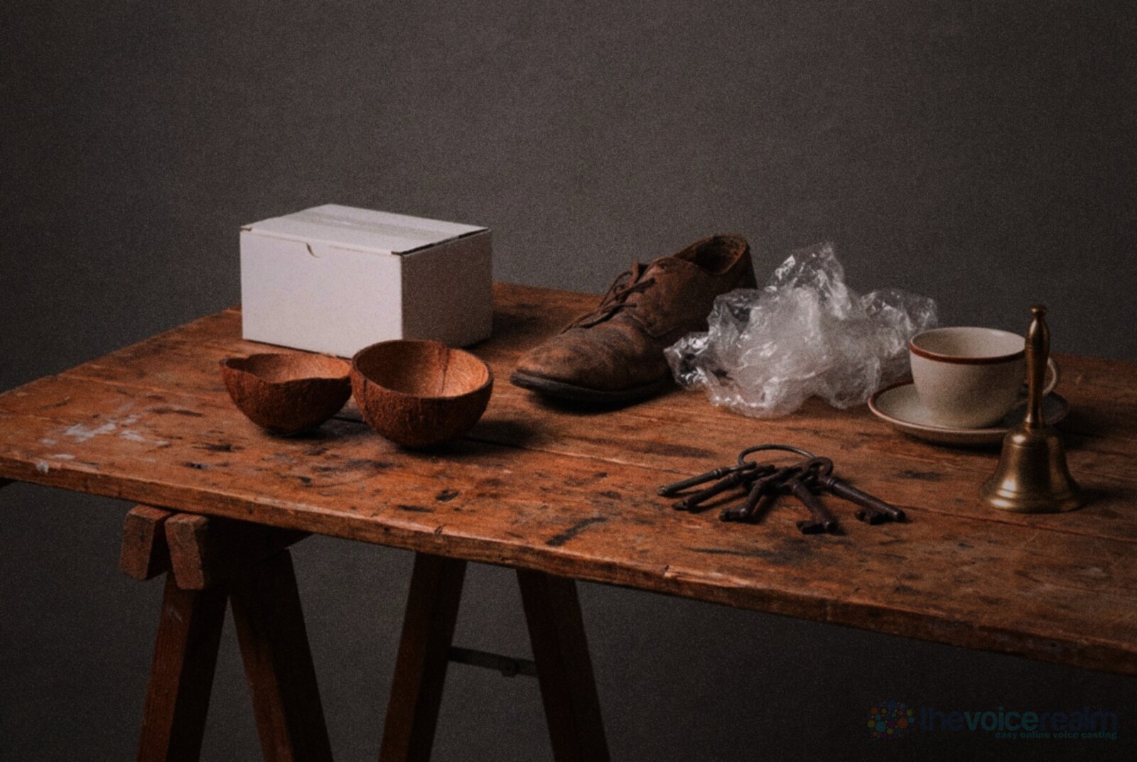 A trestle table of radio drama sound effect props: two coconut shell halves, a plain white box, an old leather shoe, crumpled cellophane, a ring of iron keys, a teacup and a brass hand bell © The Voice Realm