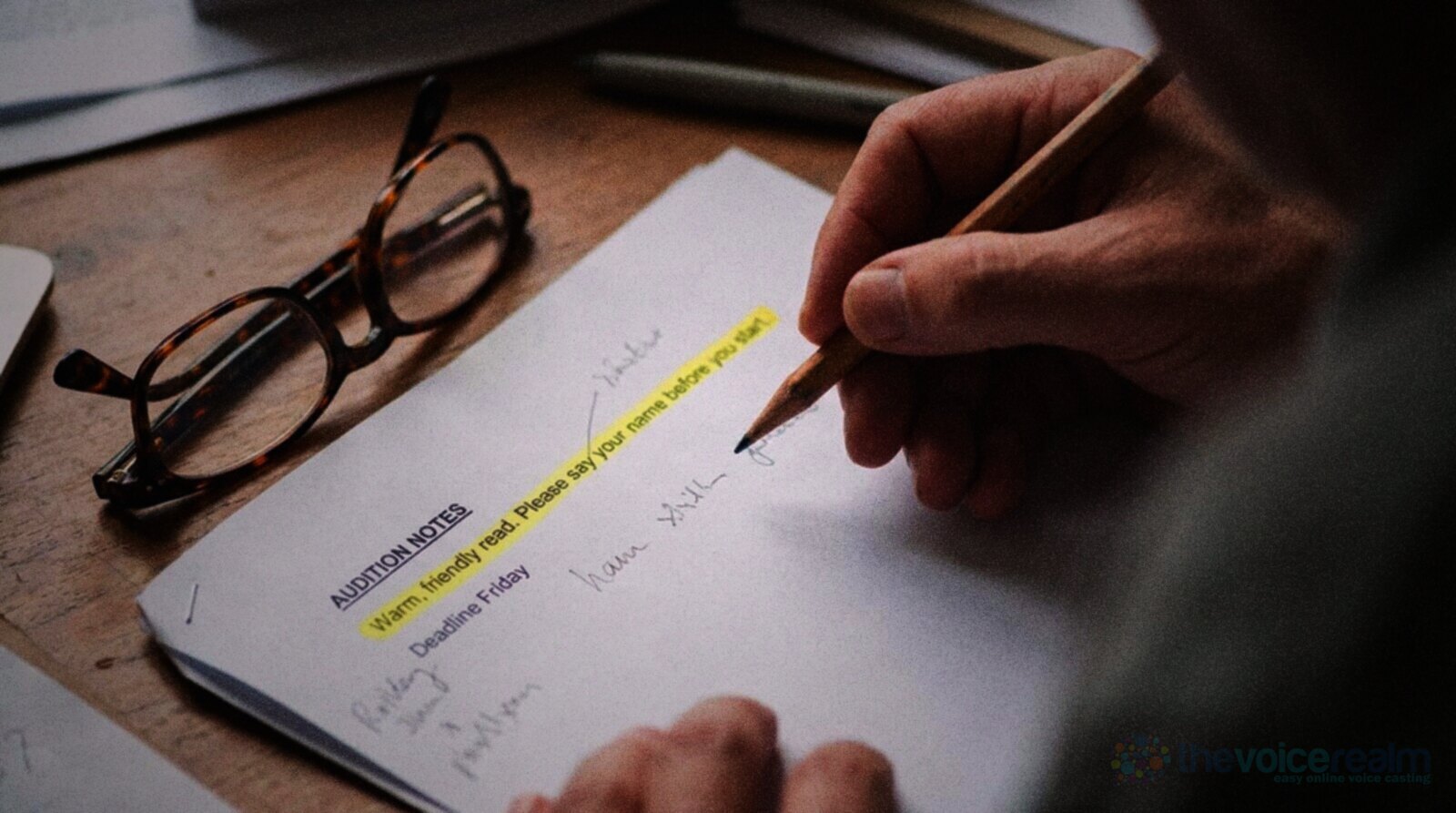 Close up of a hand with a pencil over a printed page headed Audition Notes with the line Warm, friendly read. Please say your name before you start highlighted in yellow, reading glasses beside it © The Voice Realm