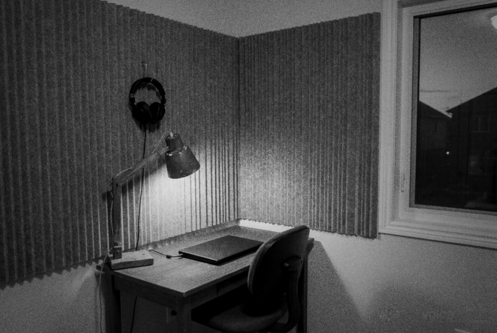 An empty home voice-over booth at dusk in black and white, headphones hanging on the acoustic panels and a closed laptop on the desk. © The Voice Realm