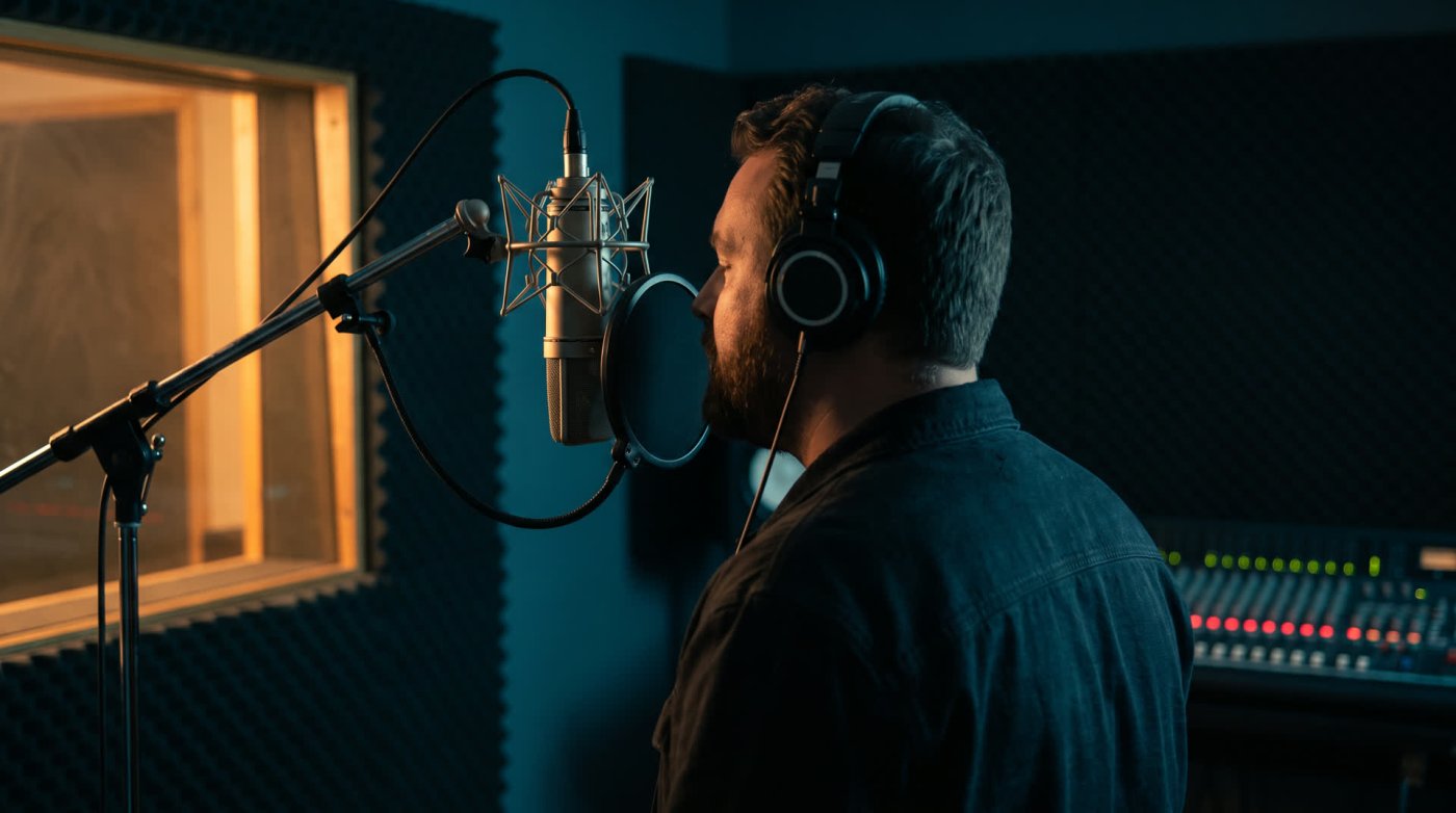 A voice actor wearing headphones recording at a studio microphone